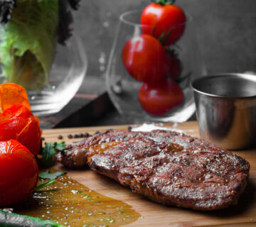 Bife de vista lateral com tomate e papel e molho picante na placa de bife 360x320